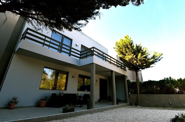 A modern two-story building with a balcony, large windows, and potted plants. - Lilies Villa (Rhodes)
