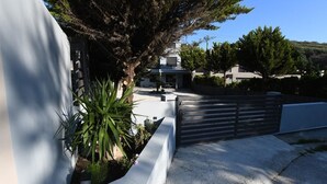 Un edificio moderno con entrada protegida, un jardín bien cuidado con un árbol grande y una vista despejada del paisaje circundante.