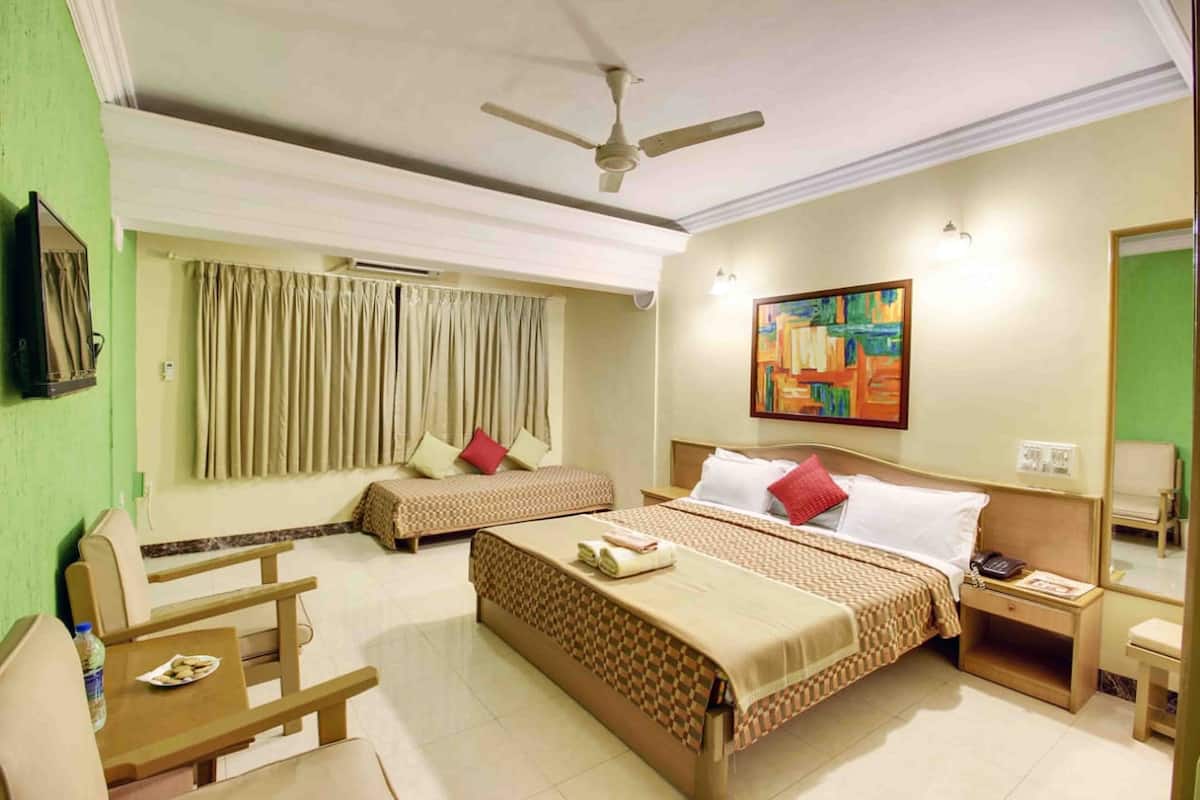 A hotel room with two beds, a desk, a chair, a ceiling fan, a painting, and a mirror.