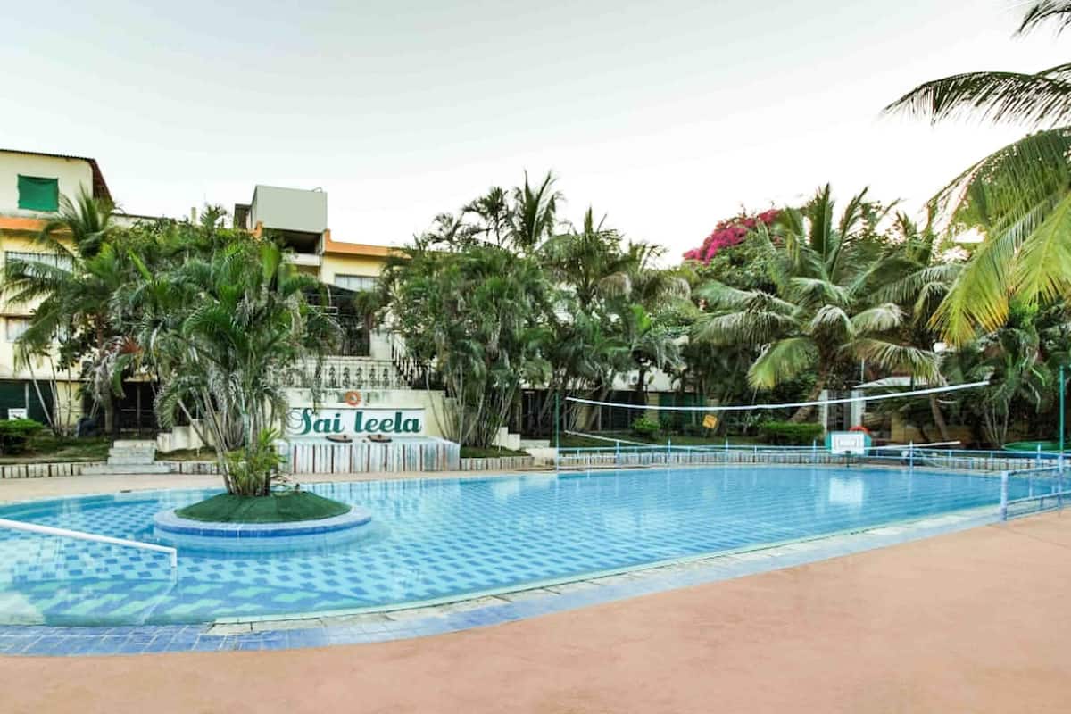 A swimming pool with a tiled deck, surrounded by palm trees and a sign that reads "Sai leela".