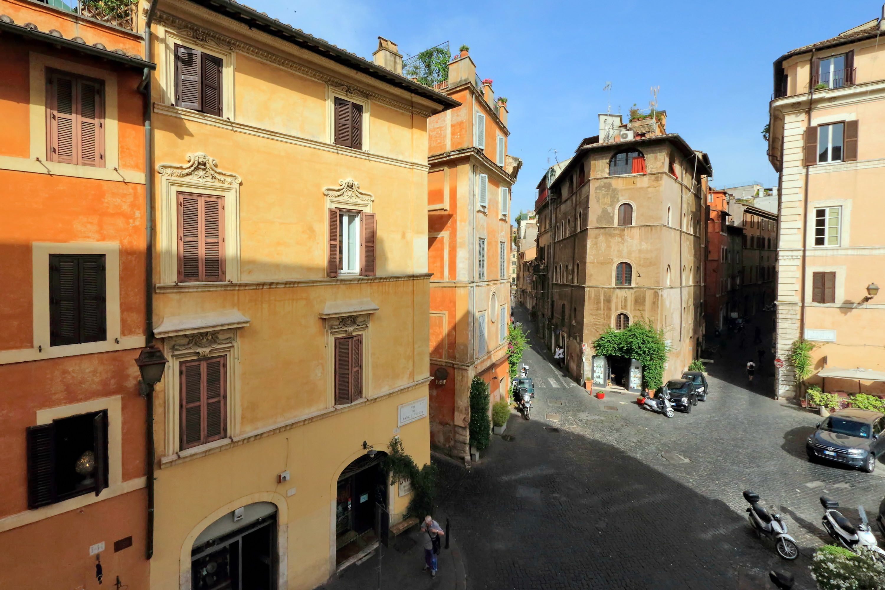 A narrow street lined with historic buildings, featuring a mix of architectural styles and a few parked vehicles.