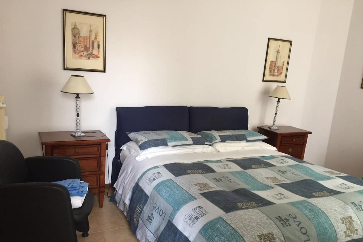 A bedroom with a bed, two nightstands, a chair, and two wall-mounted lamps.
