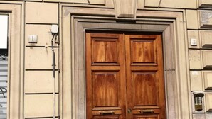 A double wooden door with a brass handle, flanked by beige stone walls and a sign above reading "Largo S. Alfonso". - La Capitale B&B (Rome)