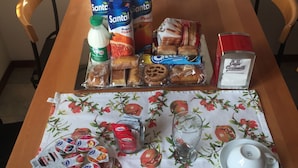 A dining table set with a floral tablecloth, a fruit bowl, various packaged foods, and a teapot. - La Capitale B&B (Rome)