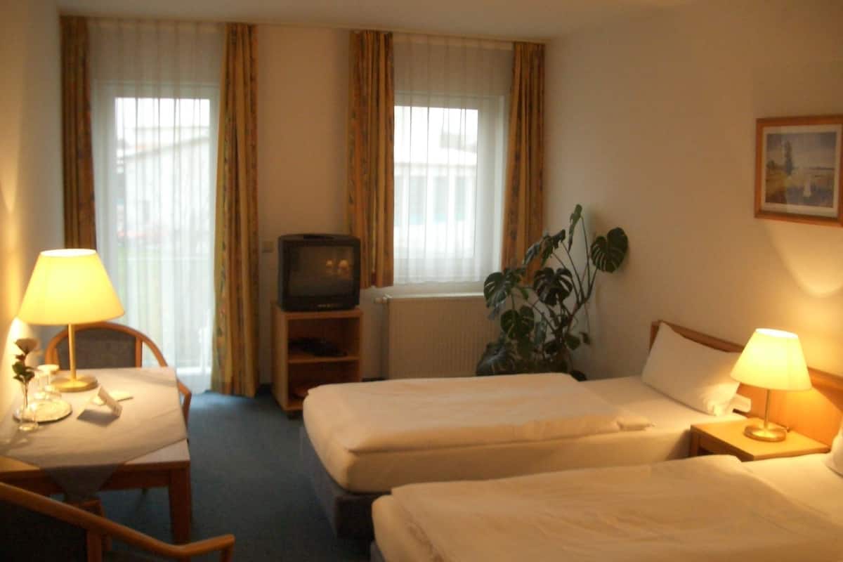 A hotel room with two beds, a television, a desk with a lamp, and a plant.