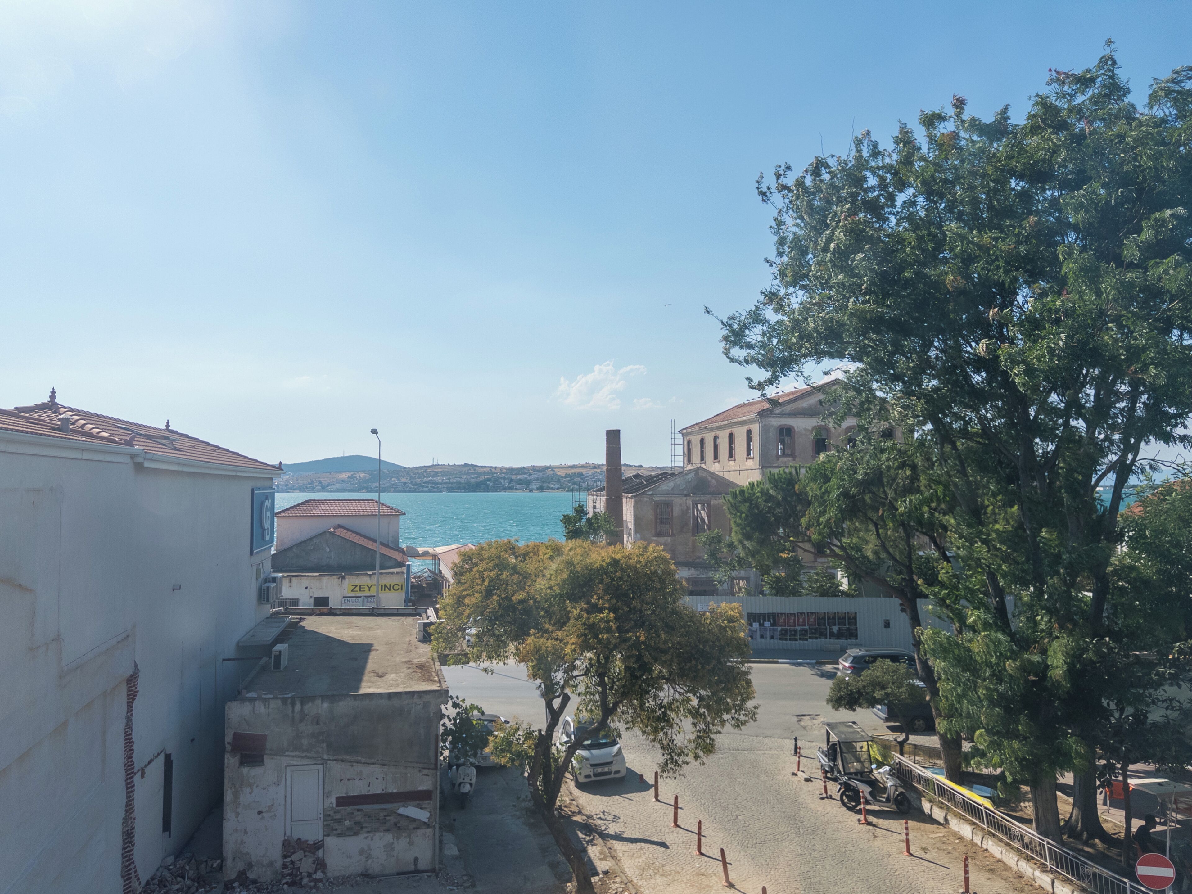 A coastal town with buildings, a tree-lined street, and a view of the sea.