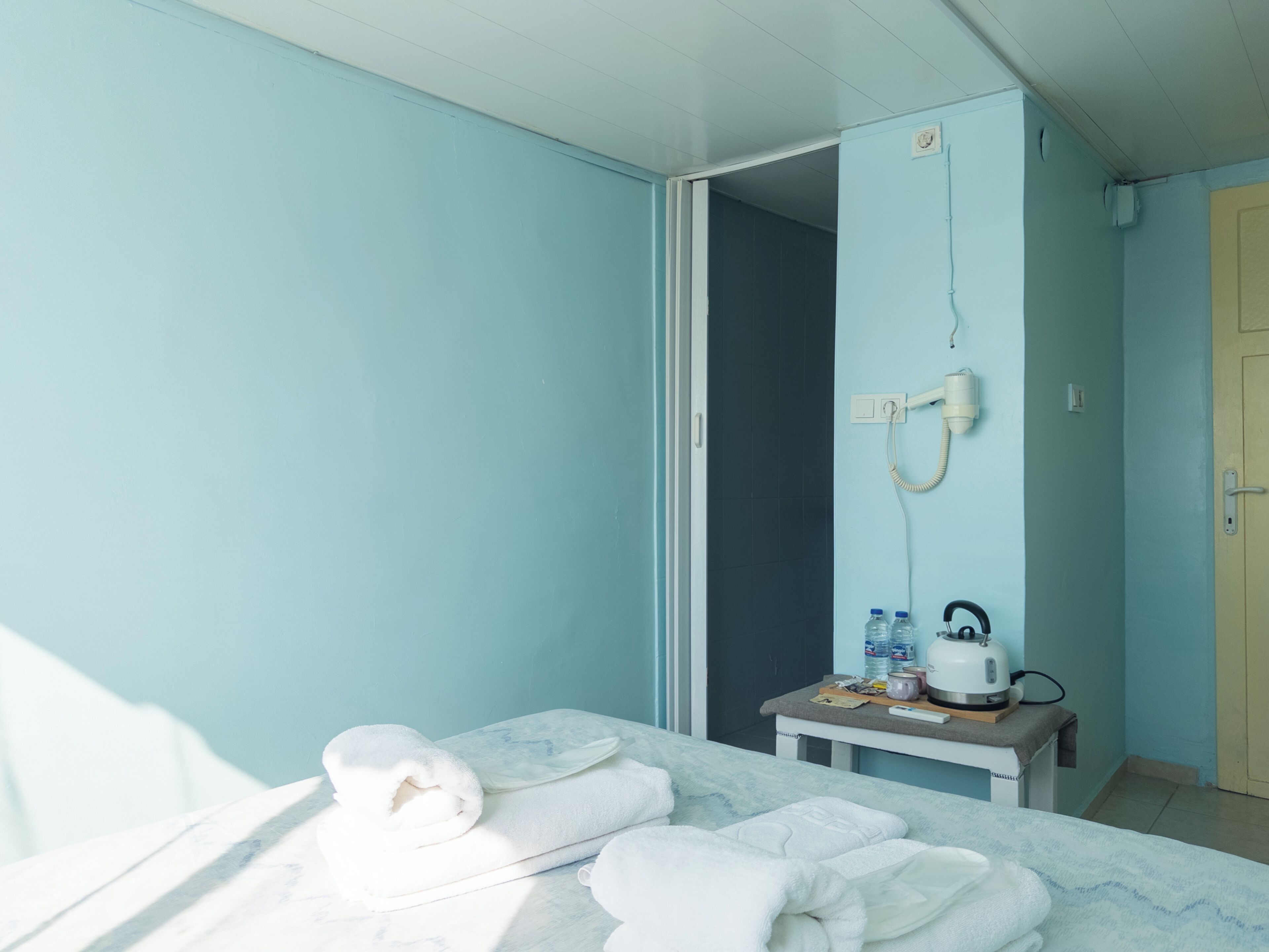 Una habitación con una cama, una pequeña mesa con artículos de aseo, zona de ducha y una puerta.