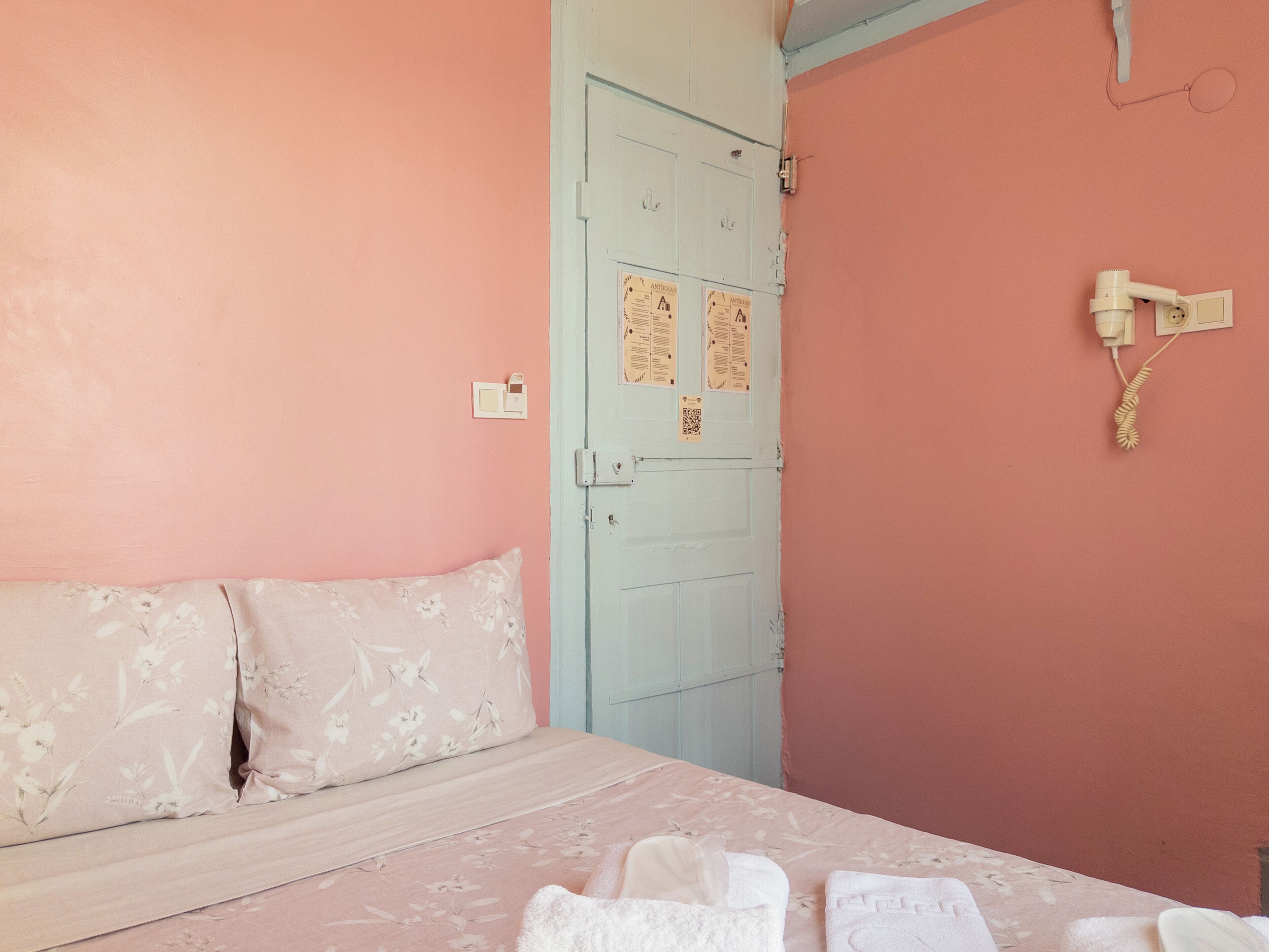 A bedroom with a bed, pillows, a door, and a wall-mounted phone.