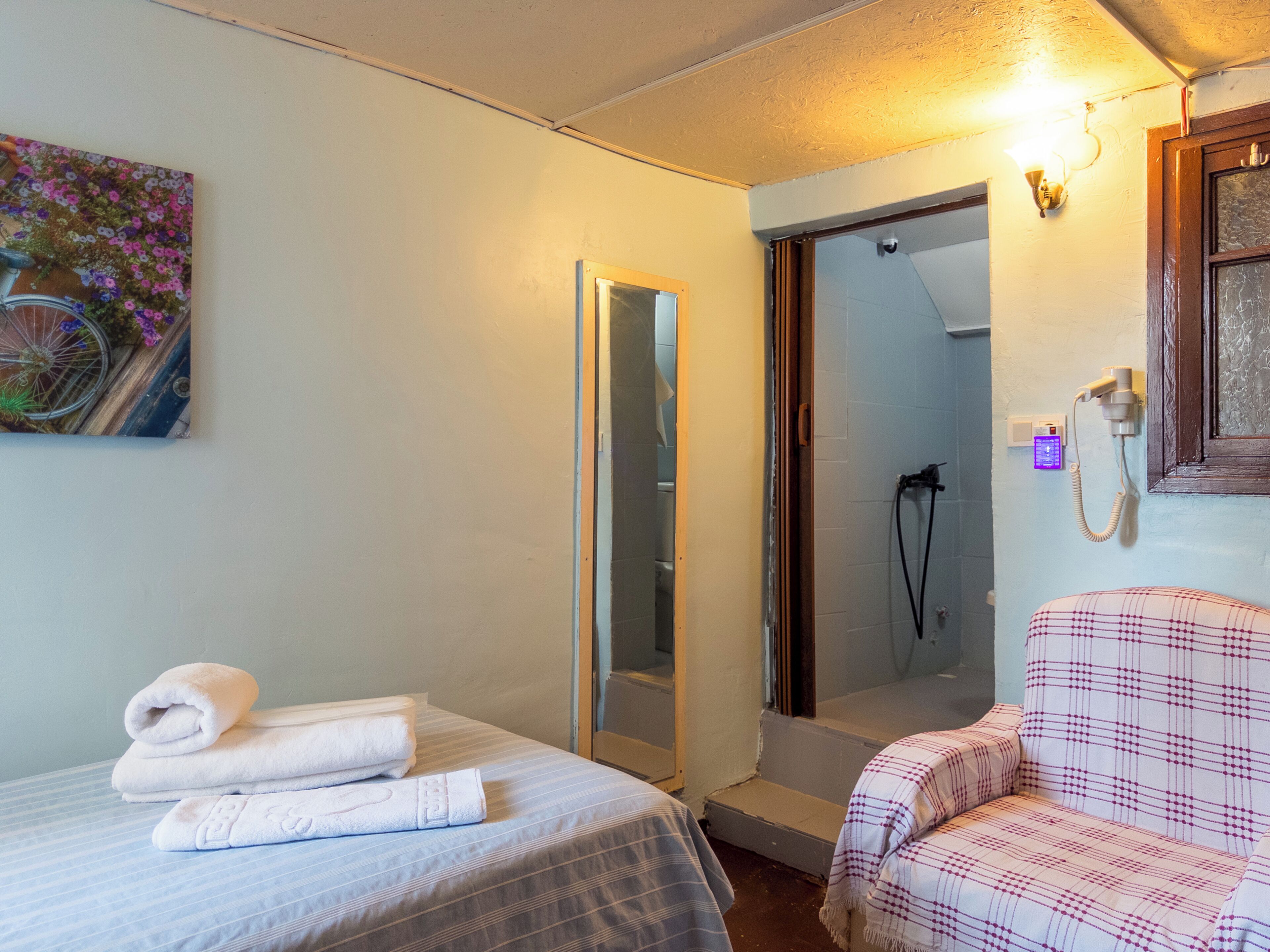 Een hotelkamer met een bed, een stoel, een douche en een spiegel in de badkamer.