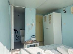 A room with a bed, a small table with a kettle, a wardrobe, and a bathroom with a shower and toilet. - Tarihi Rum Konağı Antikhan (Ayvalik)