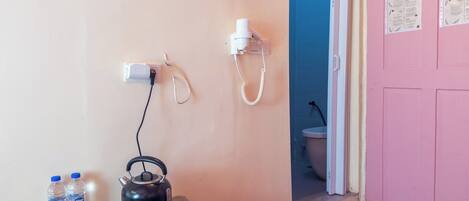A room with a pink door, a table with a kettle, water bottles, and a remote control.