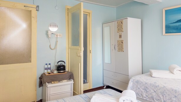 A hotel room with a bed, a wardrobe, a desk with a kettle, a mirror, and a door with a frosted glass panel. - Tarihi Rum Konağı Antikhan (Ayvalik)