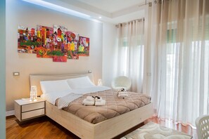 Un dormitorio moderno con una cama grande, una mesita de noche, una silla y una ventana con cortinas traslúcidas.
