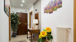 Un pasillo con una planta en maceta, un escritorio con lámpara, un jarrón con flores y un radiador.