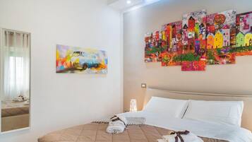 Quarto de hotel com uma cama, um quadro de um carro e um mural colorido de casas.