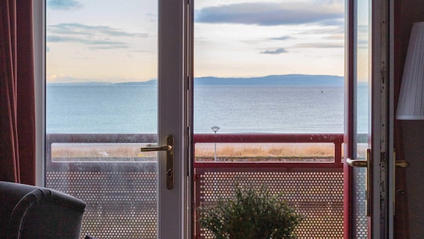 A room with a view of the sea through a door, a table with a blue tray, and a potted plant. - Bay View - Donnini Apartments (Ayr)