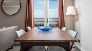 A hotel room with a wooden dining table, a round mirror, a sofa, and a view of the sea through a glass door. - Bay View - Donnini Apartments (Ayr)