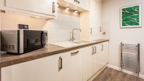 A modern kitchen with white cabinets, a stainless steel sink, and a microwave on the counter. - Bay View - Donnini Apartments (Ayr)