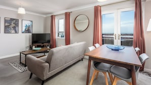A modern living room with a sofa, TV, dining table, and chairs. - Bay View - Donnini Apartments (Ayr)
