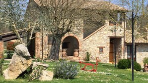 A stone house with a large tree in the front yard, a red sculpture, and a stone bench. - Azienda Agrituristica I Tre Casali (Magione)