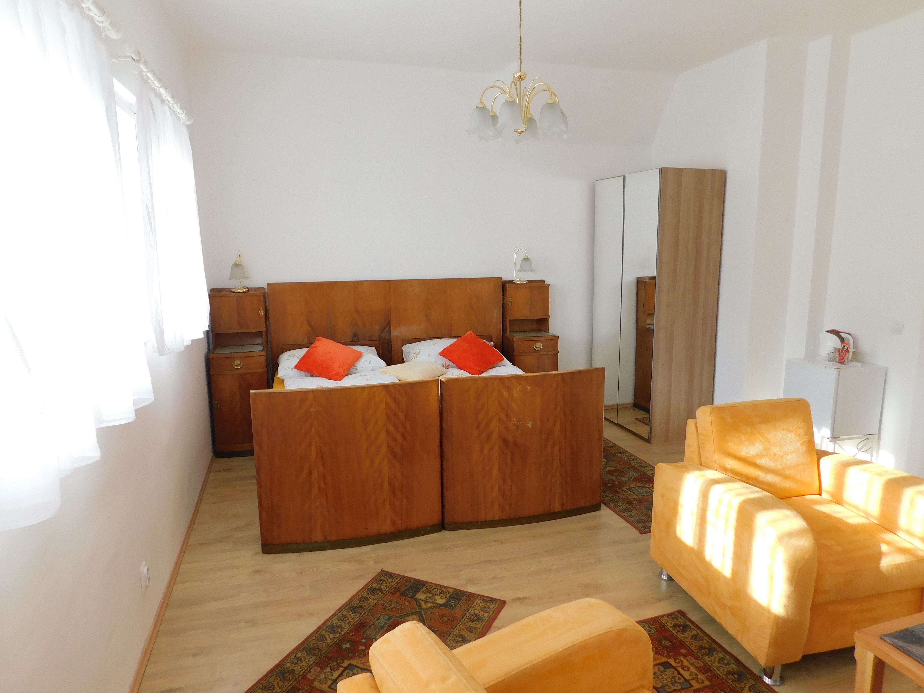 A bedroom with a wooden bed, two bedside tables, a mirror, a yellow armchair, and a patterned rug.