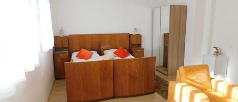 A bedroom with a wooden bed, two bedside tables, a mirror, a yellow armchair, and a patterned rug.