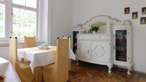 A dining room with a white table set for four, a white cabinet with glass doors, and a window with a view of greenery. - Vila Arnau (Hostinne)