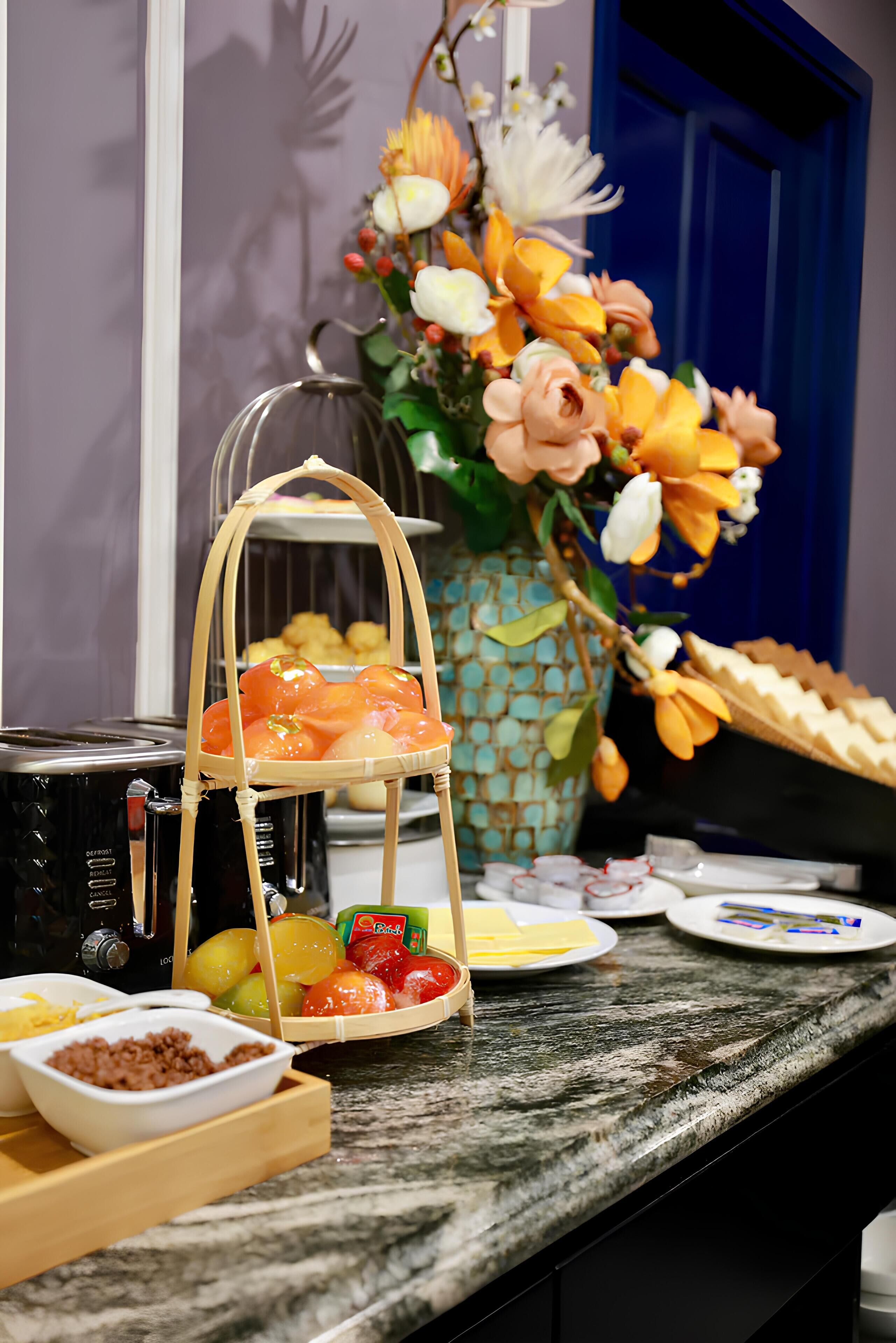 A kitchen counter with a fruit basket, a vase with flowers, and various kitchen appliances.