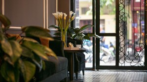 A room with a sofa, a small table with a vase of flowers, and a view through a window with a metal gate. - Matilda Boutique and Spa Hotel (Hanoi)