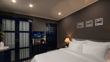 A hotel room with a large bed, a TV mounted on the wall, a desk with a lamp, and a wardrobe.