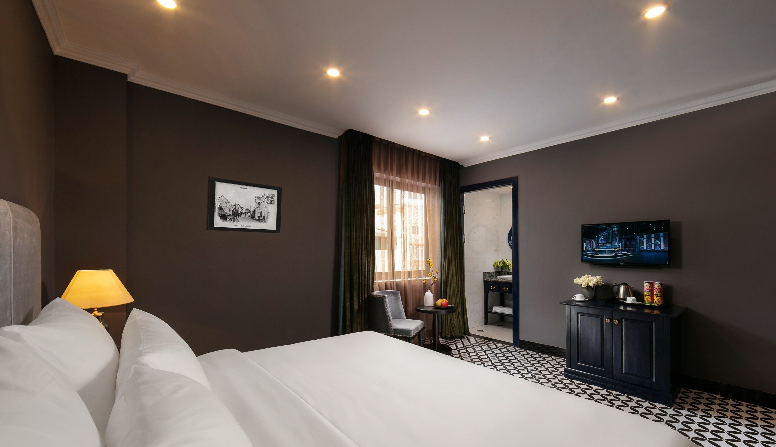 A hotel room with a large bed, a desk with a TV, a chair, and a window with curtains.