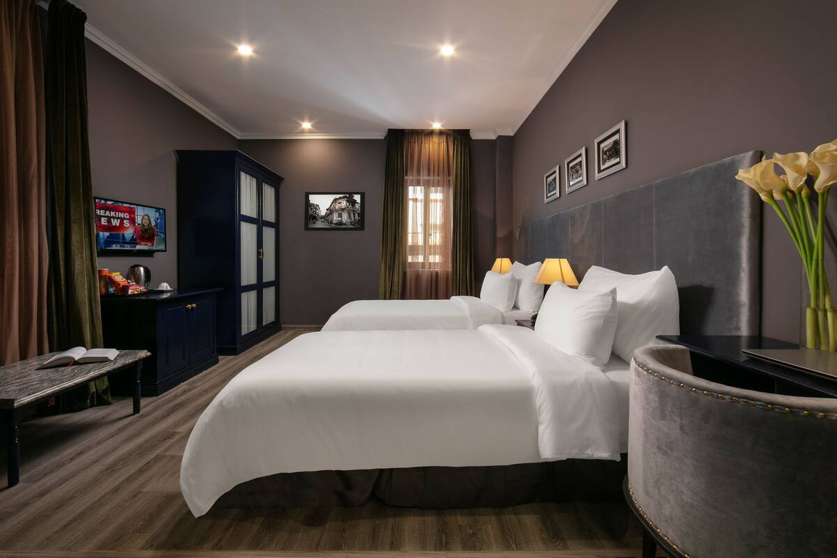 A hotel room with a double bed, a desk, a chair, a TV, a cabinet, and a window with curtains.