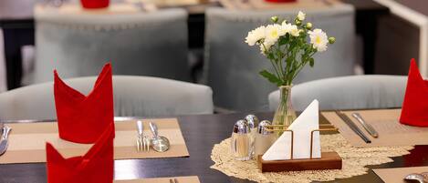 A dining table set with red napkins, silverware, a vase with white flowers, and a small sailboat model.