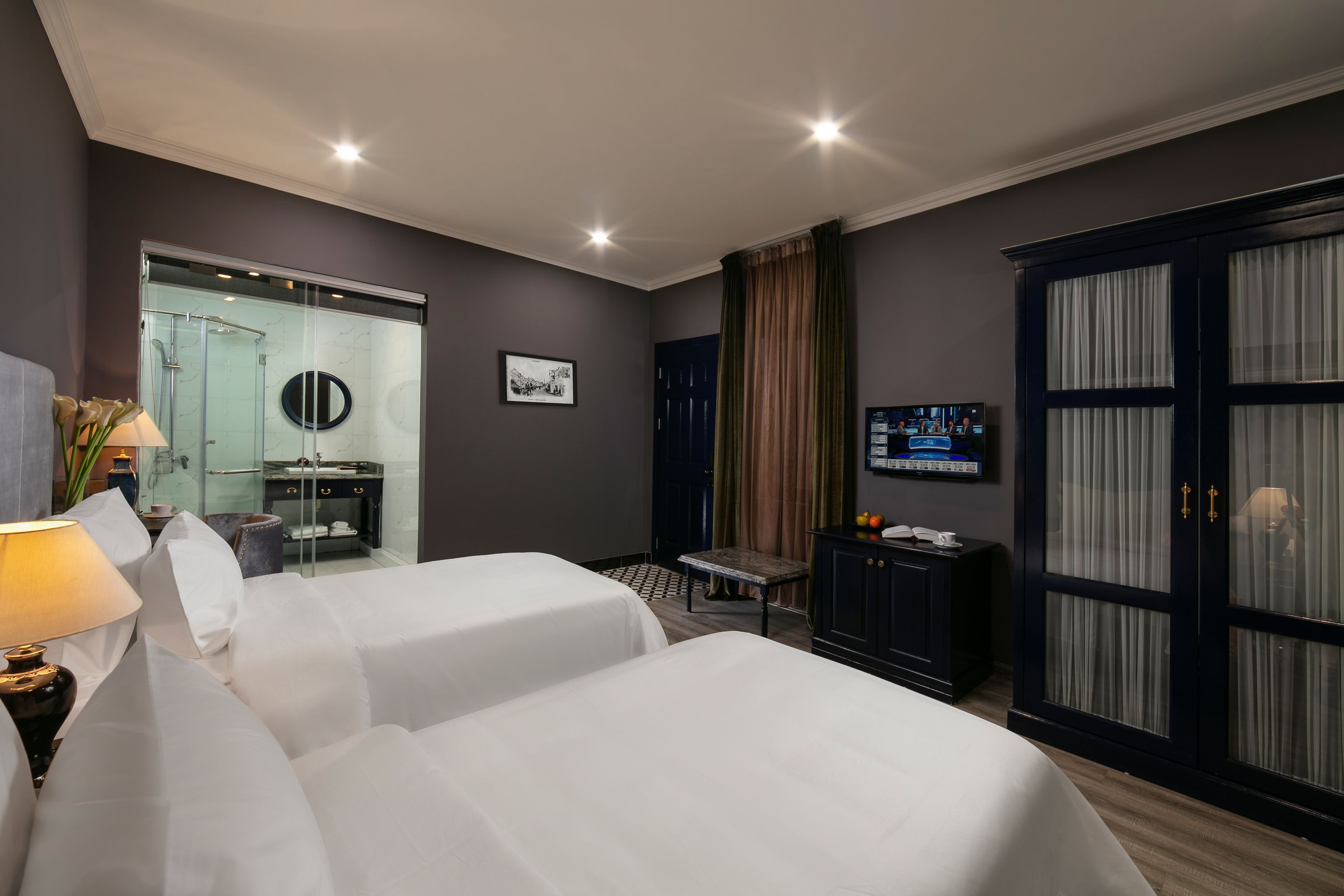A hotel room with two beds, a bathroom, a TV, and a desk with a lamp.