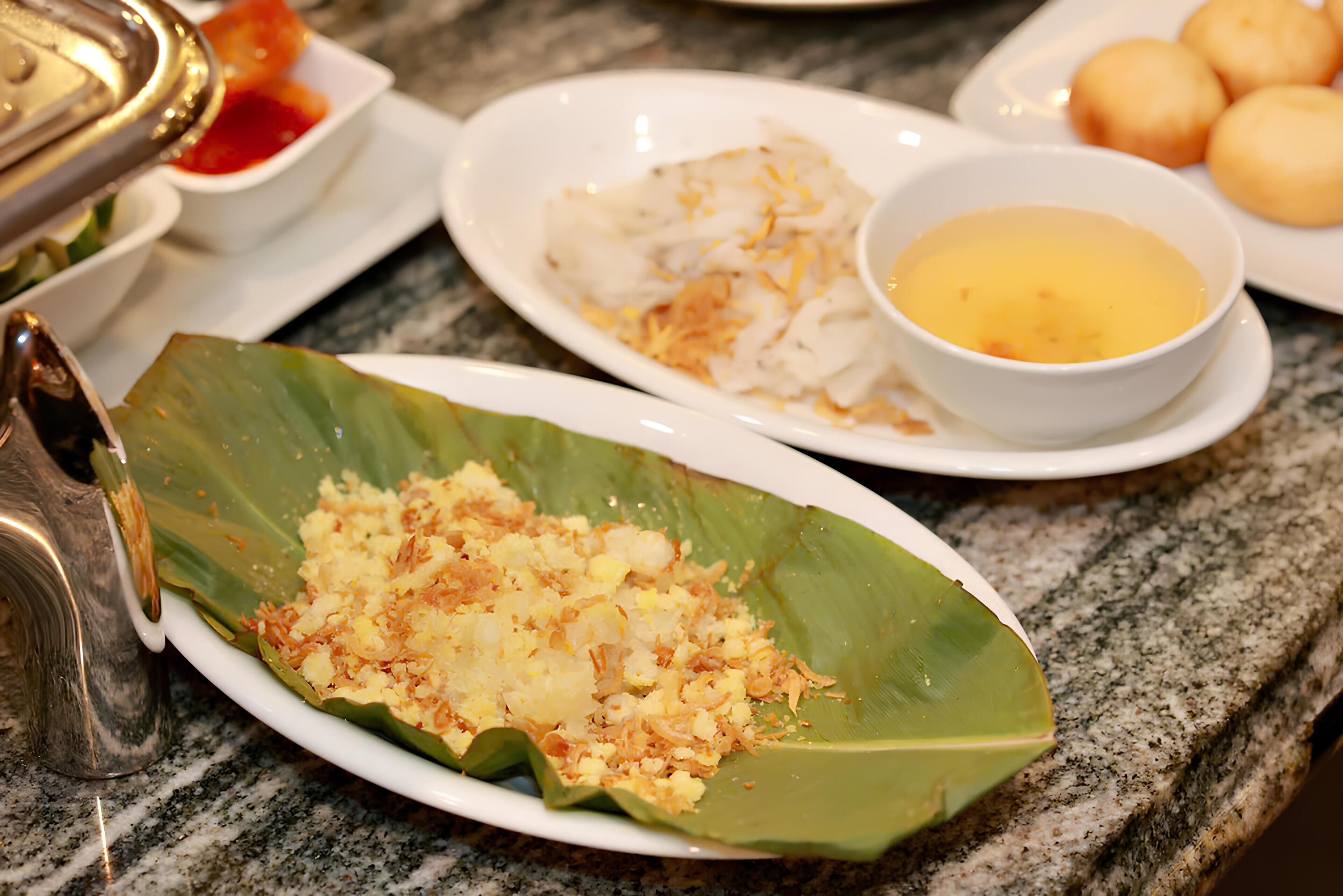 Una mesa con varios platos, incluyendo un plato servido sobre hoja de plátano, un tazón de sopa y algunos dumplings.