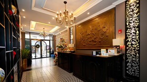 A hotel reception area with a chandelier, a reception desk, a large decorative wall, and a patterned floor. - Matilda Boutique and Spa Hotel (Hanoi)