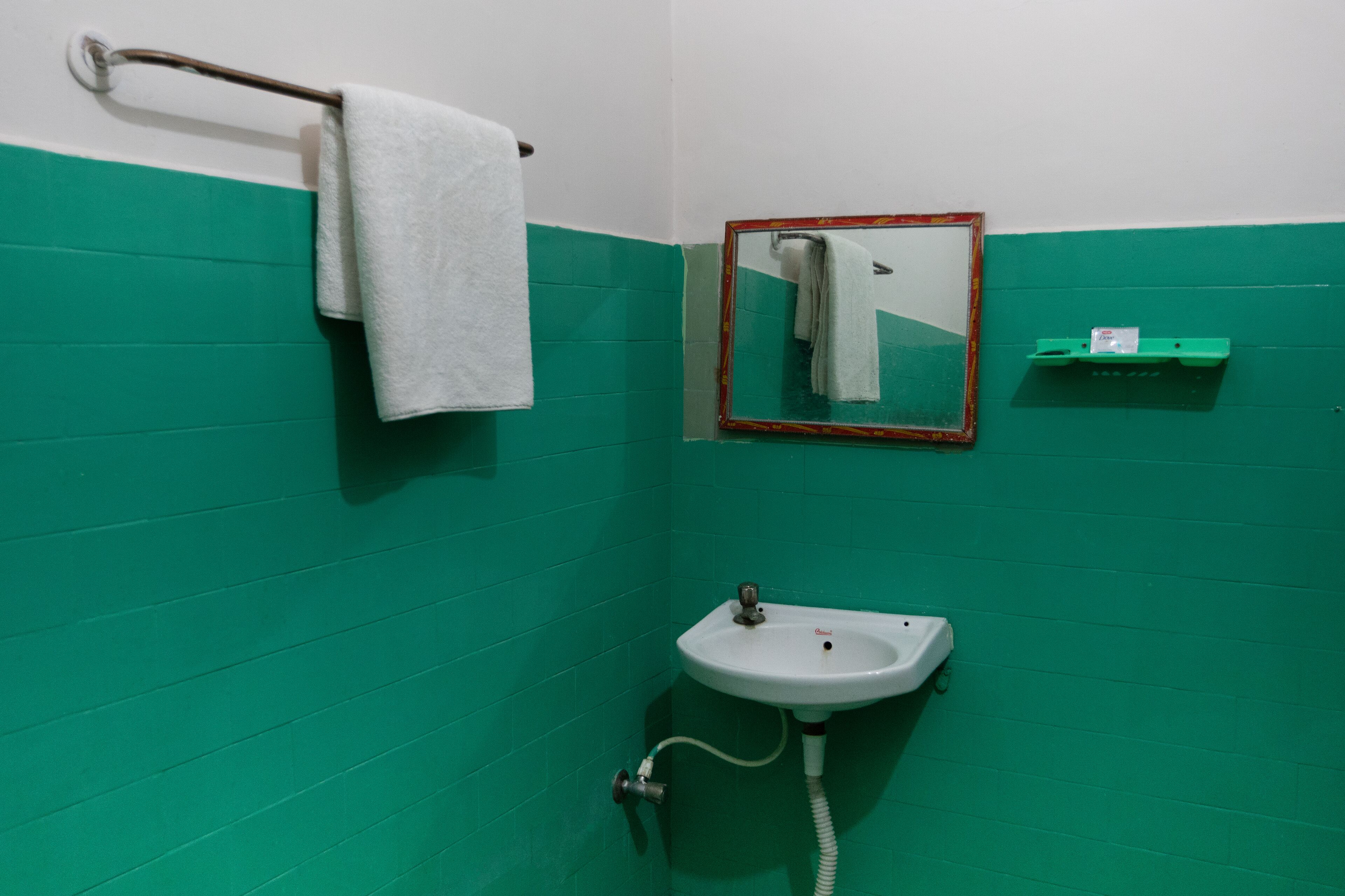 A bathroom with a green tiled wall, a white sink with a mirror above it, and a towel hanging on a metal rack.