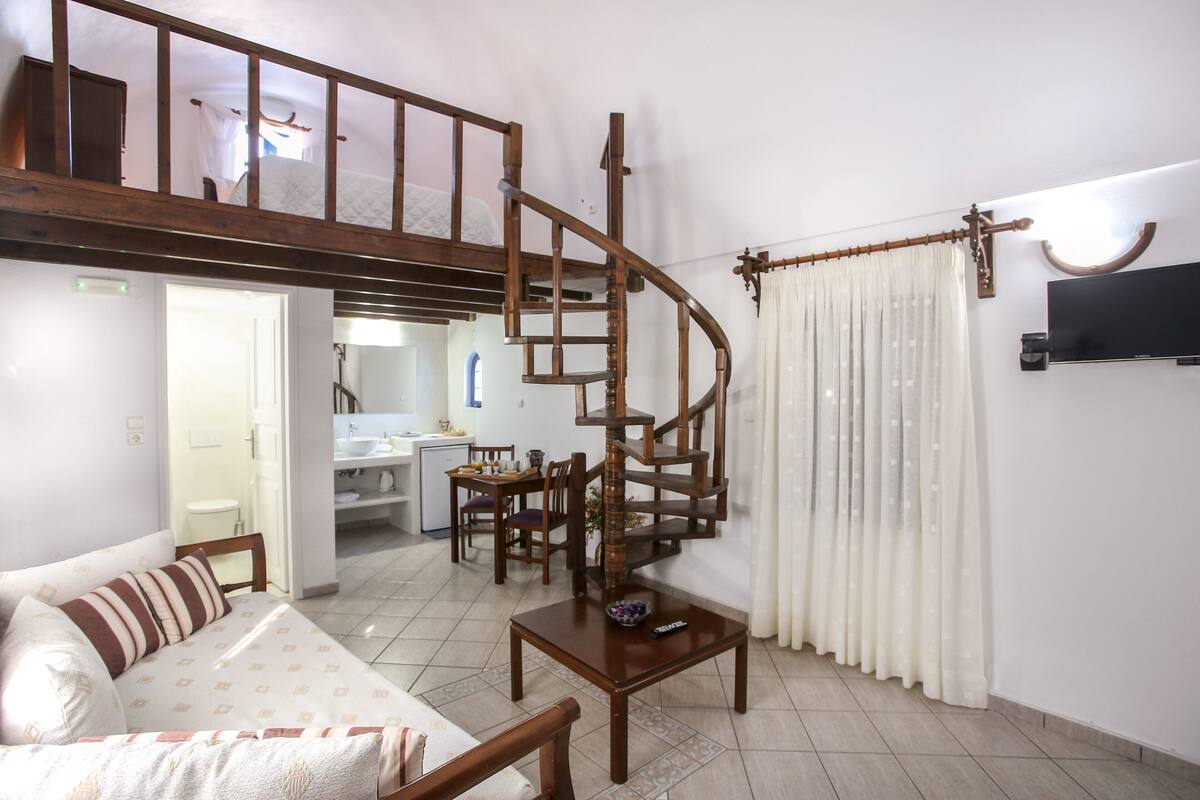 A living room with a wooden spiral staircase, a sofa, a dining table, and a kitchen area in the background.