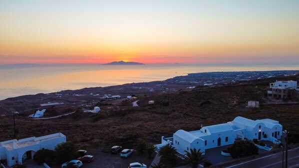 A coastal village with white buildings, a clear view of the sea, and a sunset in the background.