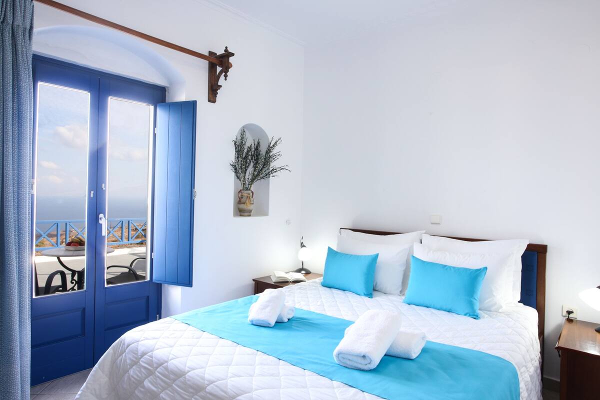 A hotel room with a bed, a nightstand, a window with a view, and a door.