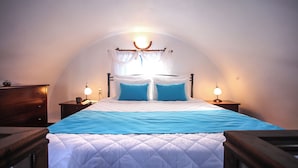 A bedroom with a bed, two bedside tables, a nightstand, a lamp, and a window with curtains.