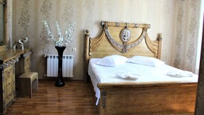 A bedroom with a wooden bed, a bedside table, a mirror, and a radiator. - Hotel Oniks (Kutaisi)
