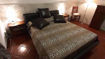 Un dormitorio con cama, mesitas de noche, una silla y una lámpara.
