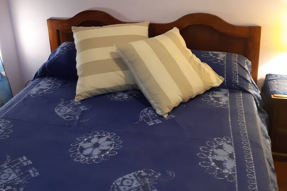 A bed with a blue patterned bedspread, two pillows, and a wooden headboard.