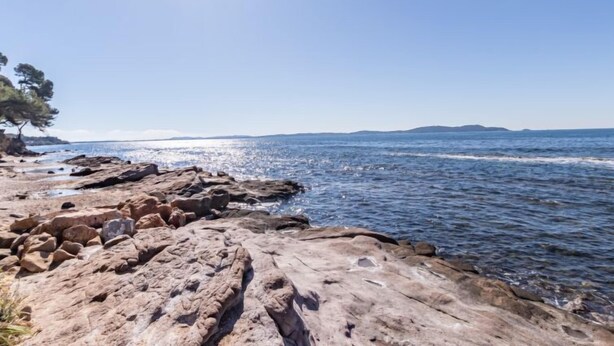 A rocky shoreline with clear blue water and distant landforms. - Les Jardins d'Hélios by Interhome (Carqueiranne)