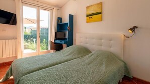 A bedroom with a bed, a desk, and a chair. There is a window with curtains, a painting on the wall, and a lamp on the side. - Les Jardins d'Hélios by Interhome (Carqueiranne)