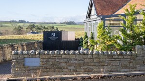 A stone wall with a sign reading "SUNNYSIDE" and a building with a glass facade. - Northern Hideaways, Sunnyside, Otterburn (Newcastle-upon-Tyne)