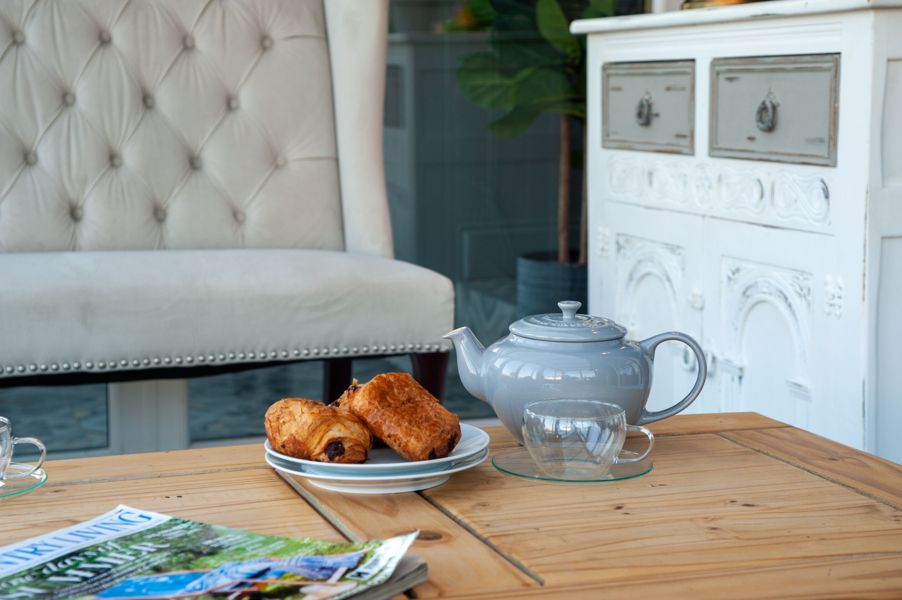 A wooden table with a teapot, a glass, and pastries on a plate.