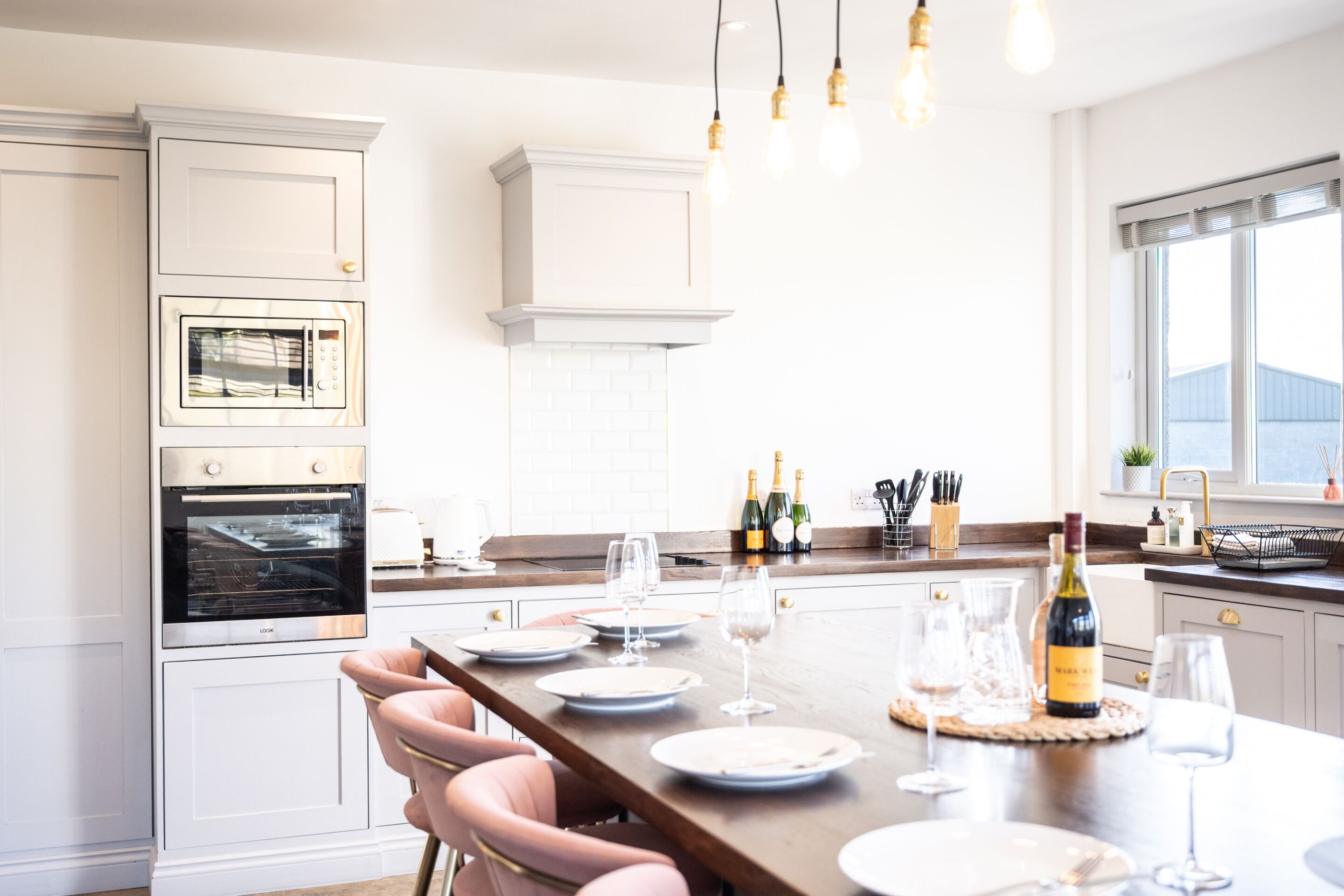 A modern kitchen with white cabinetry, a built-in oven, and a dining area set for six with a wooden table and pink chairs.