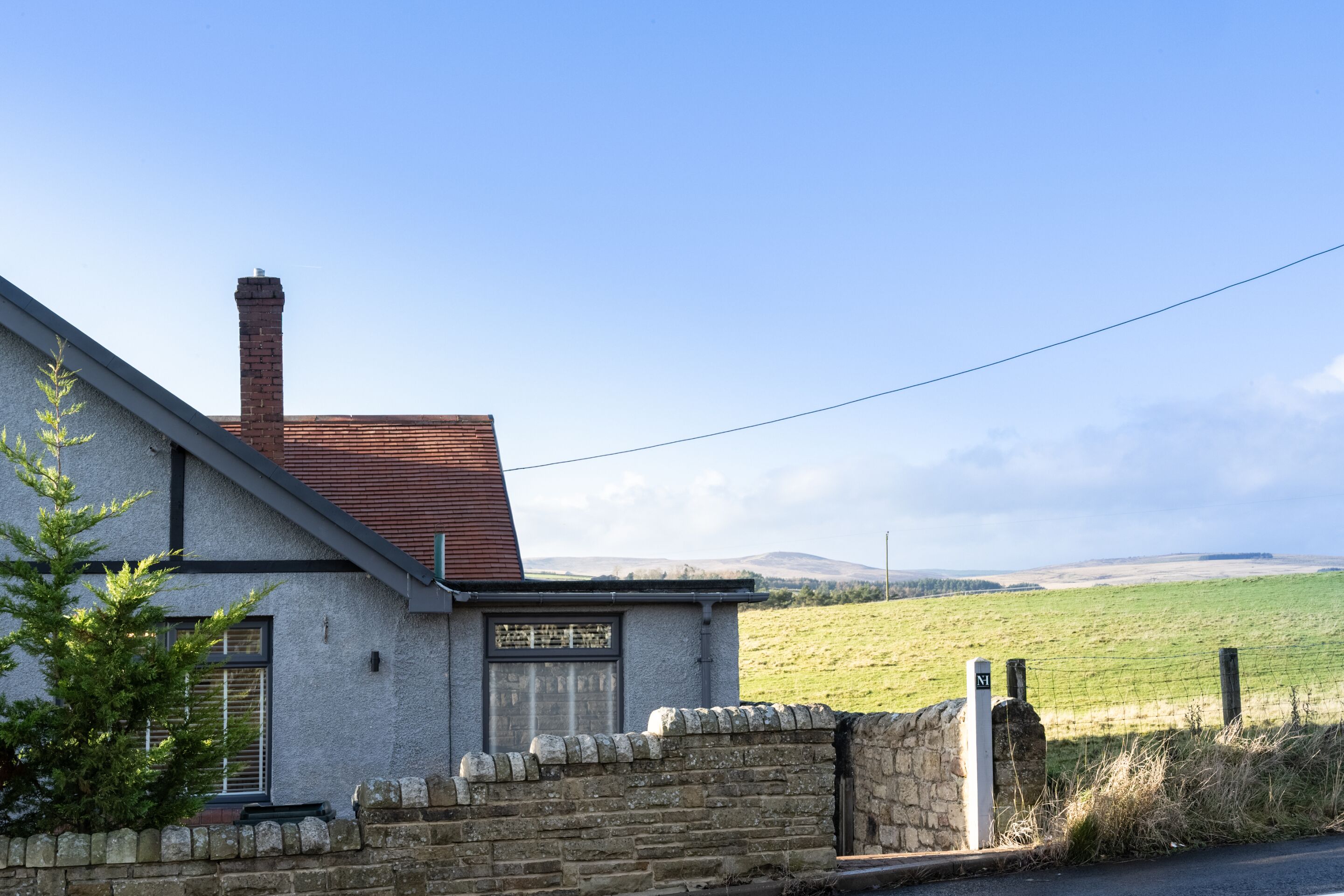 A house with a stone wall, a chimney, and a view of a green field.